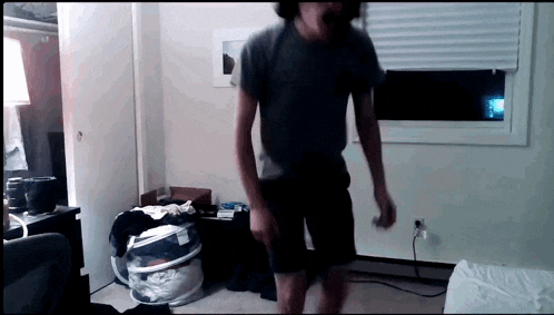 a man in a grey shirt is dancing in a room