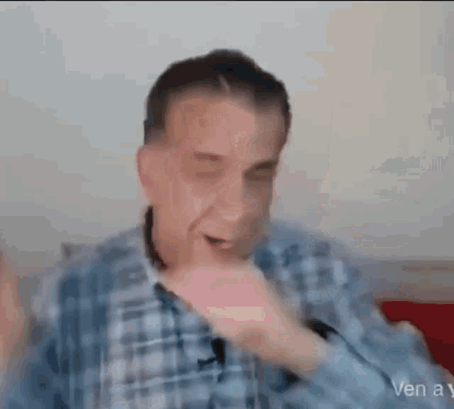 a man in a plaid shirt is making a funny face with his hand .