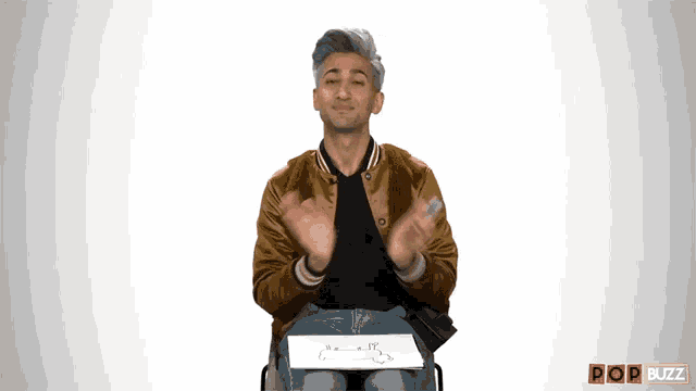a man in a brown jacket is sitting in front of a sign that says popbuzz