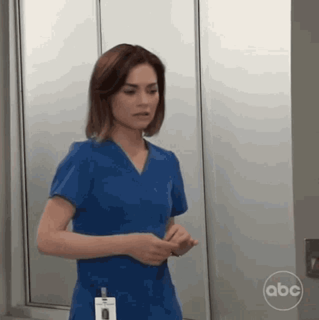 a woman in a blue scrub top is standing in a room with a abc logo on the wall .