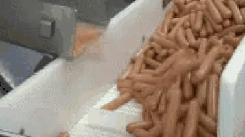 a conveyor belt filled with sausages is being loaded into a machine .