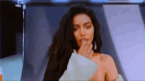 a woman with long hair is covering her mouth with her hand while looking at the camera .