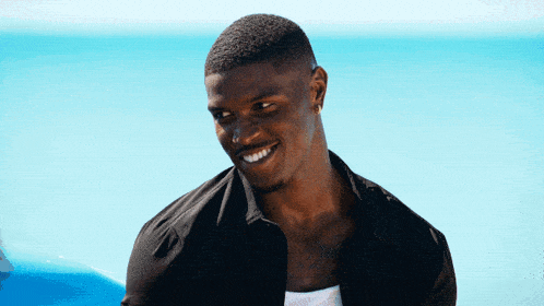 a man wearing a black shirt is smiling in front of the ocean