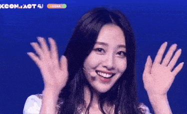 a woman is smiling and waving her hands in front of a microphone on a stage .