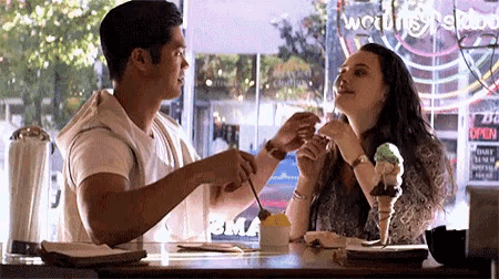 a man and a woman are sitting at a table with ice cream cones in front of a sign that says " open "