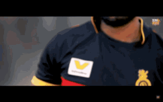 a close up of a man wearing a black shirt with a yellow v on it