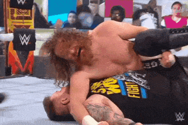 a wrestler wearing a shirt that says ' fight ' on it is wrestling another wrestler