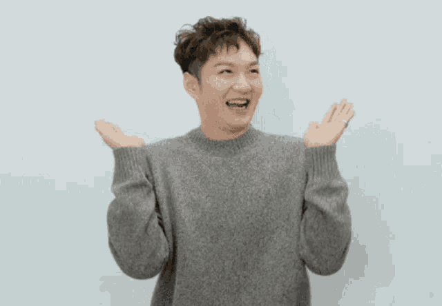 a man wearing a grey sweater is laughing with his hands in the air