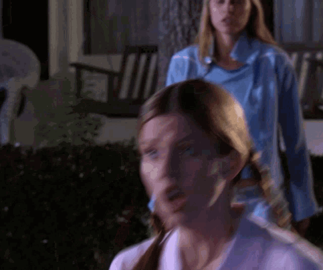 a woman in a blue shirt stands in front of a woman in a white shirt