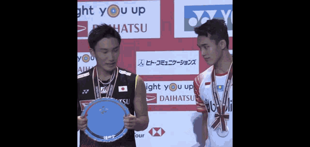 two badminton players holding a trophy in front of a sign that says light you up