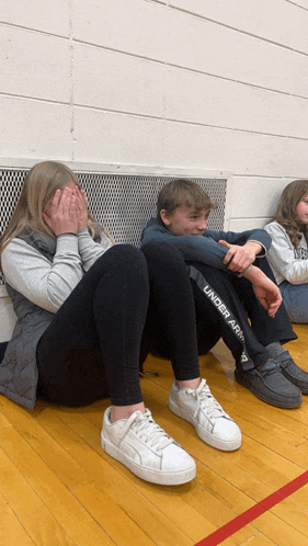 a boy wearing under armour pants sits next to a girl covering her face