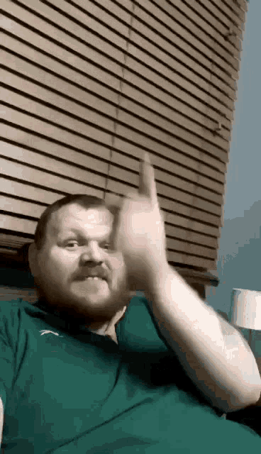 a man with a beard and mustache wearing a green puma shirt is giving the middle finger