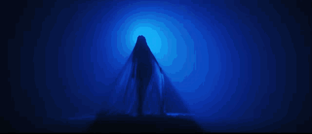a silhouette of a person standing in a dark room with a blue light behind them