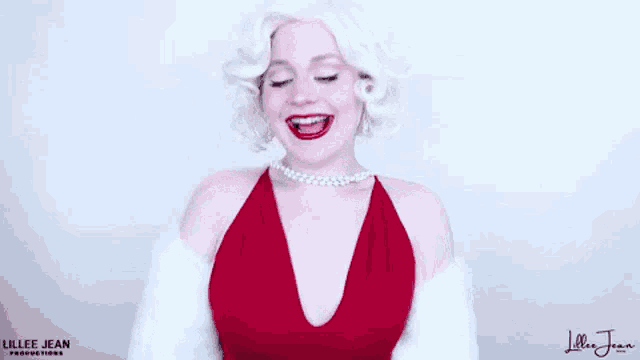 a woman is wearing a red dress and pearls and smiling