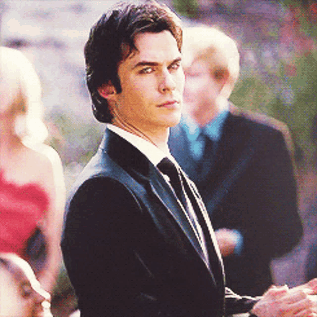 a man in a suit and tie stands in a crowd of people