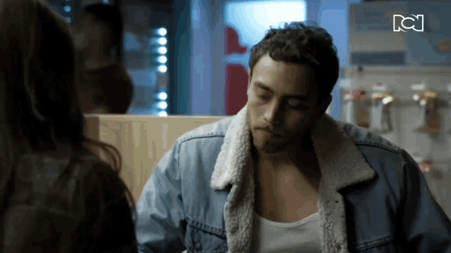 a man in a denim jacket is talking to a woman in a store
