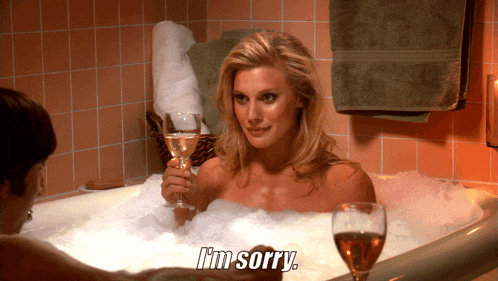 a woman in a bathtub is holding a glass of wine and says i 'm sorry