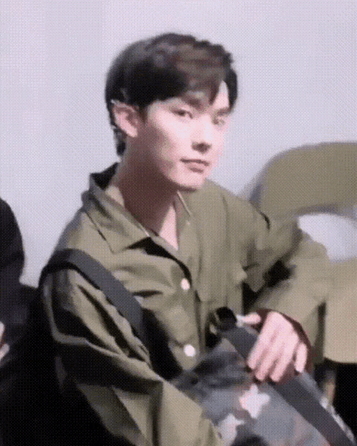 a young man in a green shirt is holding a black bag .