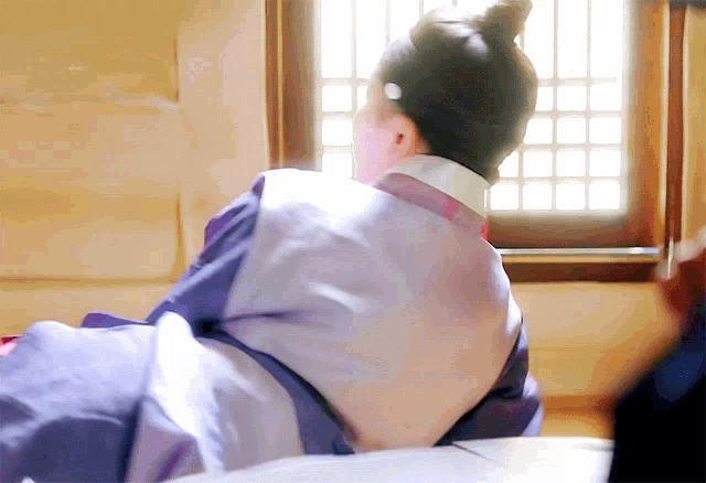 a woman in a traditional korean dress is sitting on a bed in front of a window .