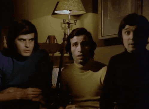 three men are sitting in front of a lamp that has the letter g on it