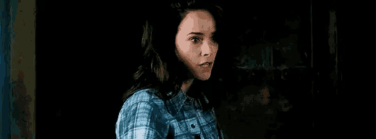 a woman in a blue plaid shirt is standing in front of a wall .