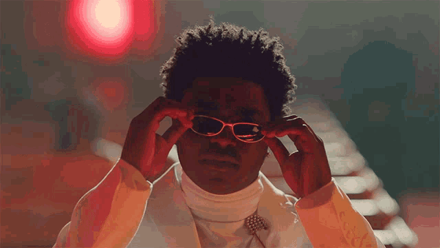 a man in a white suit is adjusting his glasses