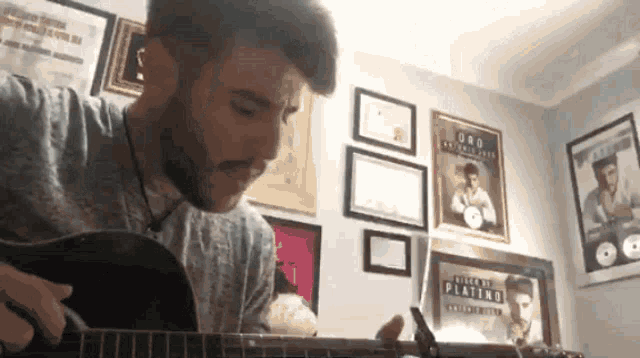 a man is playing a guitar in front of a wall with posters of elvis presley on it