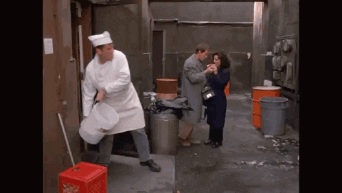 a man in a chef 's hat is holding a bucket and a woman in a black coat is standing next to him