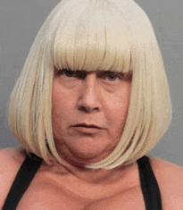 a woman wearing a blonde wig and a black bra looks at the camera