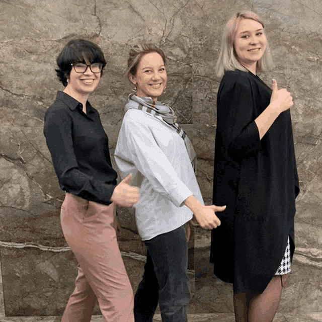 three women are posing for a picture and one gives a thumbs up
