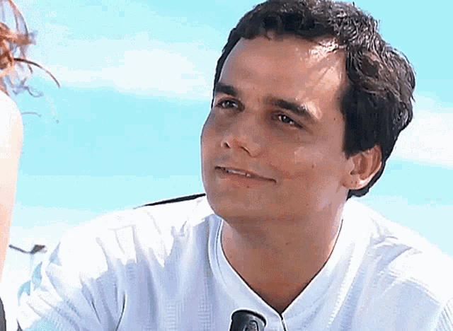 a man in a white shirt is smiling with a microphone in front of him