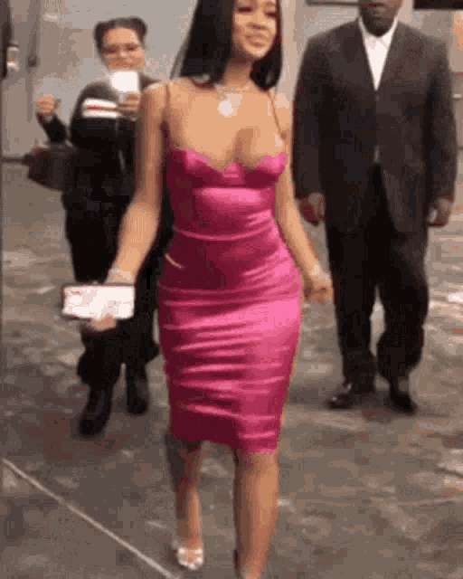 a woman in a pink dress is walking down the street with a man in a suit behind her .