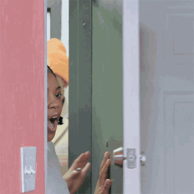 a woman is standing in front of a door with her mouth open and her hands up .