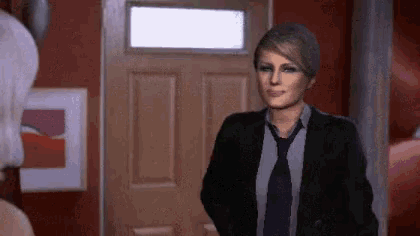 a woman in a suit and tie is standing in front of a wooden door
