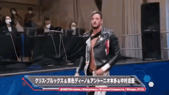 a man in a leather jacket is walking on a stage in front of a crowd