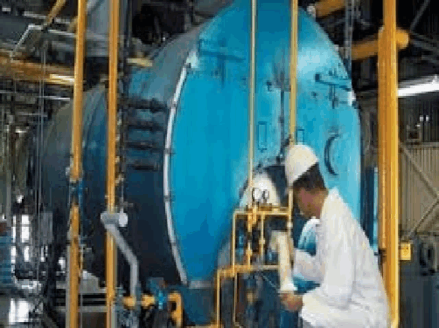 a man is kneeling down in front of a large blue boiler in a factory .