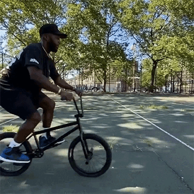 a man in a black shirt is riding a bike on a tennis court .
