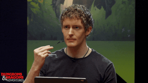 a man wearing glasses is sitting in front of a screen that says dungeons & dragons adventures