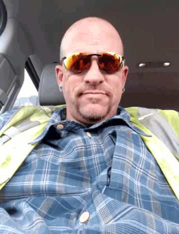a man wearing sunglasses and a safety vest is sitting in the driver 's seat of a car