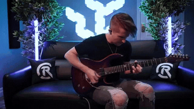 a man is playing a guitar on a couch with pillows that have letters r on them