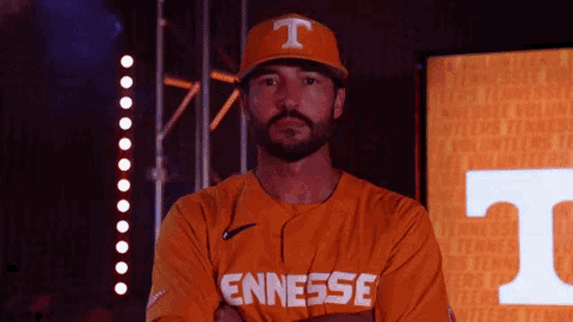 a man wearing an orange tennessee baseball jersey stands with his arms crossed