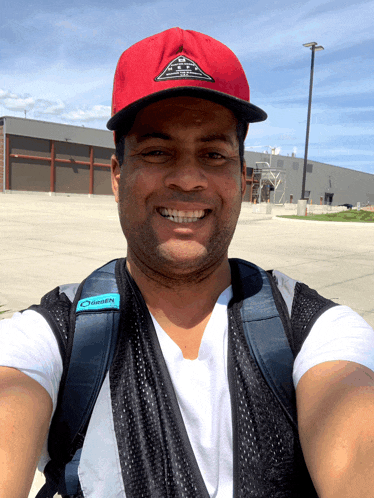 a man wearing a red hat and a black vest with the word green on it smiles