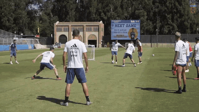 a group of soccer players are practicing on a field with a billboard behind them that says next game