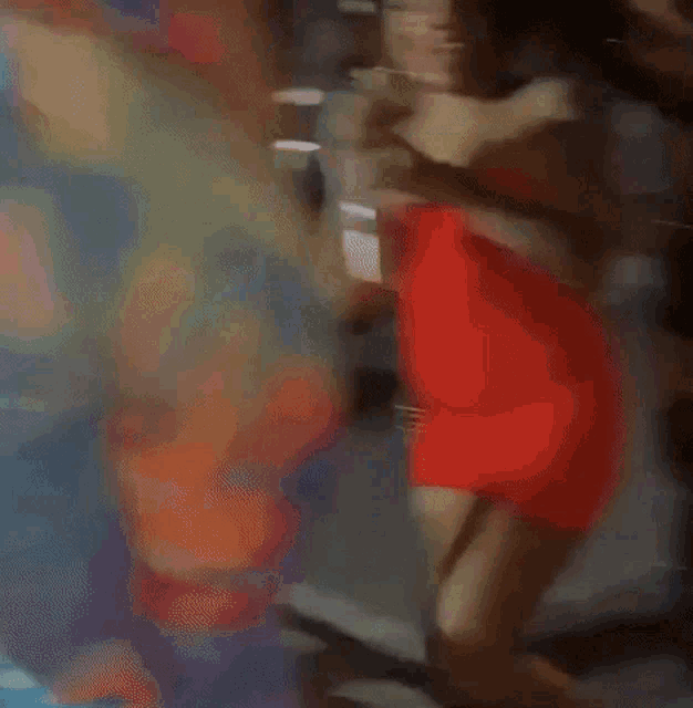 a blurry picture of a woman in a red dress dancing with a man in a colorful shirt .