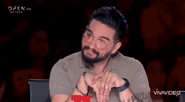 a man with a beard and glasses is sitting in front of a microphone .