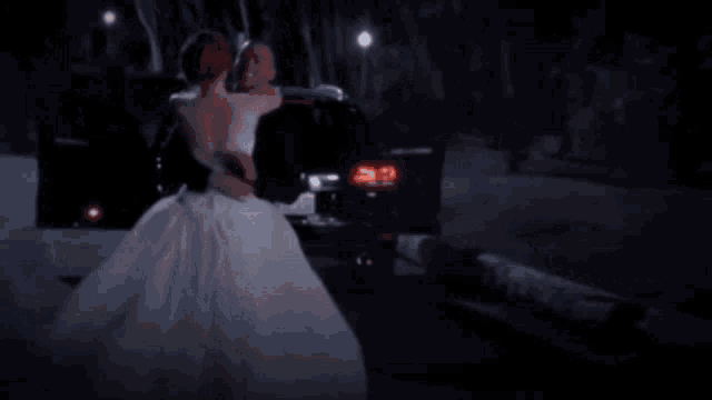 a bride and groom are dancing in front of a car at night