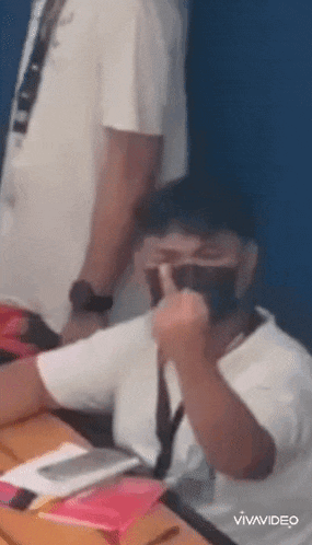 a man is standing behind a boy wearing a mask while sitting at a table .
