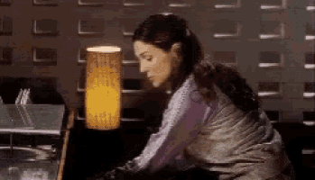 a woman in a purple shirt is sitting at a table with a lamp on it .
