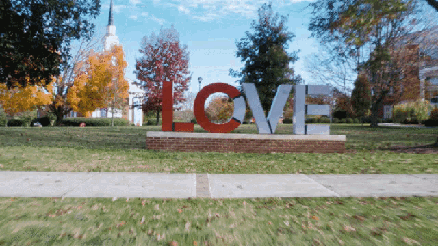 a large red and white love sign is in a park