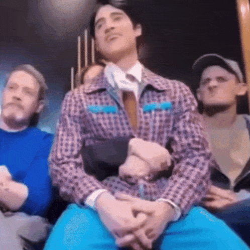 a man in a plaid shirt and tie is sitting in a crowd